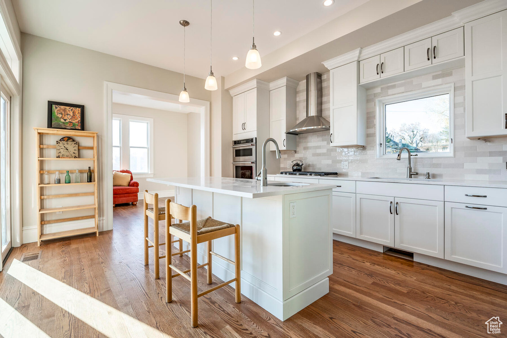 Kitchen with tasteful backsplash, light hardwood / wood-style floors, hanging light fixtures, and wall chimney exhaust hood