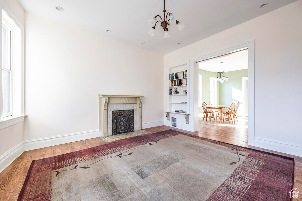 Unfurnished living room with wood-type flooring, a chandelier, a premium fireplace, and built in features