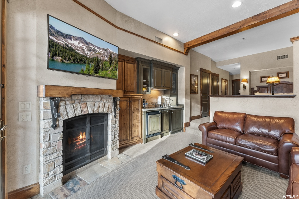 Living room with beam ceiling, a stone fireplace, and light carpet