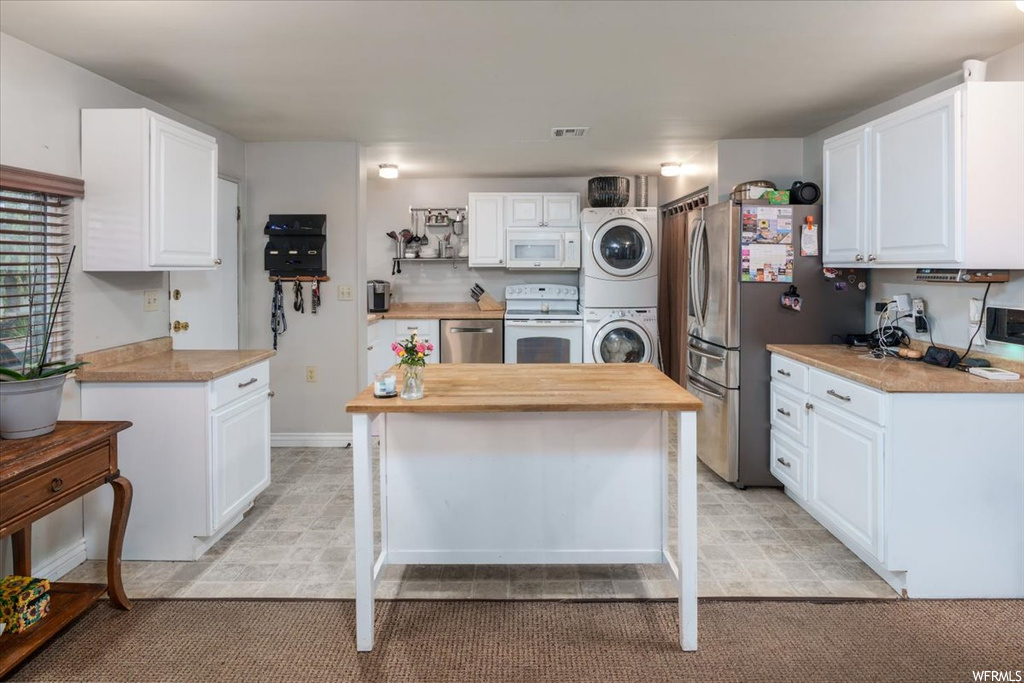 Kitchen with a center island, light carpet, stainless steel appliances, stacked washer and clothes dryer, and white cabinets