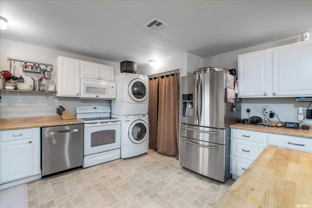 Kitchen featuring stacked washer / drying machine, white cabinets, stainless steel appliances, and light tile floors