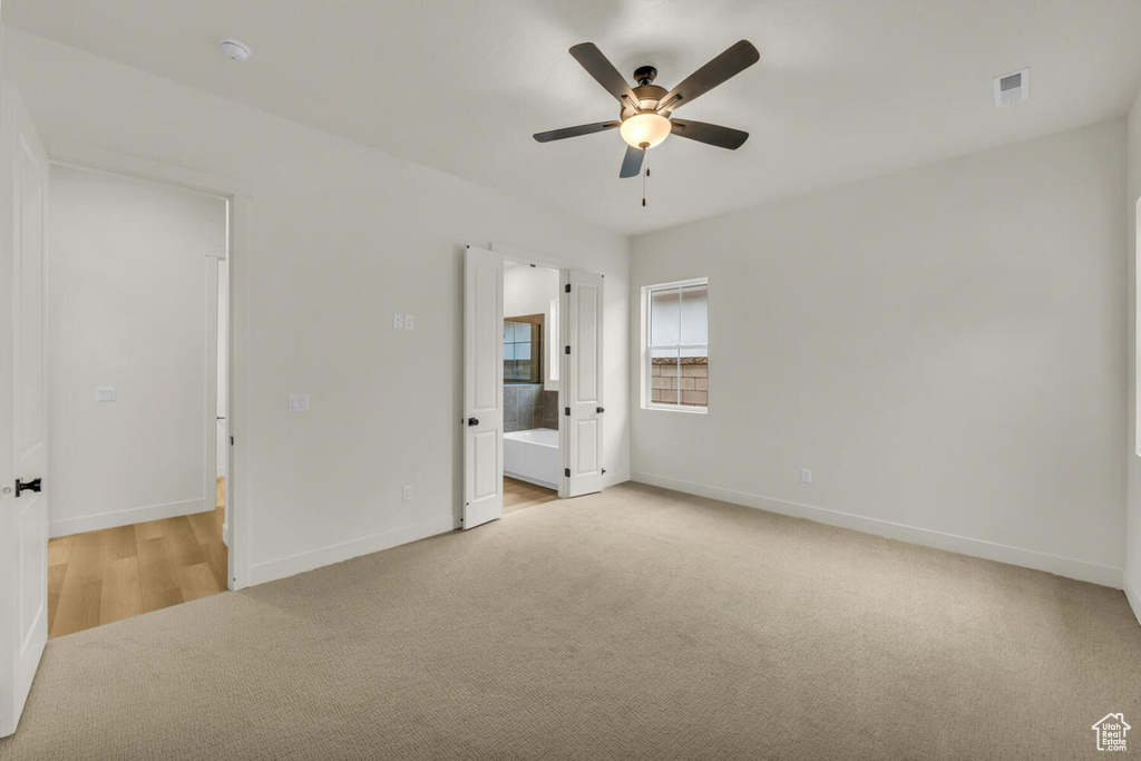 Unfurnished bedroom with light colored carpet, ensuite bath, and ceiling fan