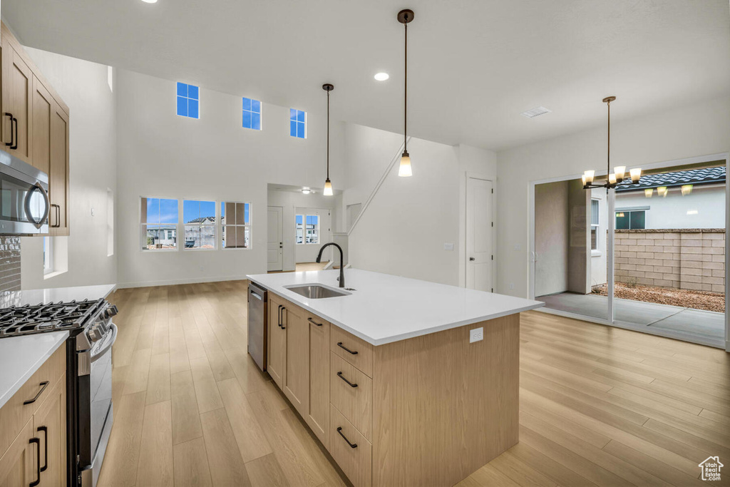 Kitchen with a center island with sink, light hardwood / wood-style flooring, appliances with stainless steel finishes, hanging light fixtures, and sink