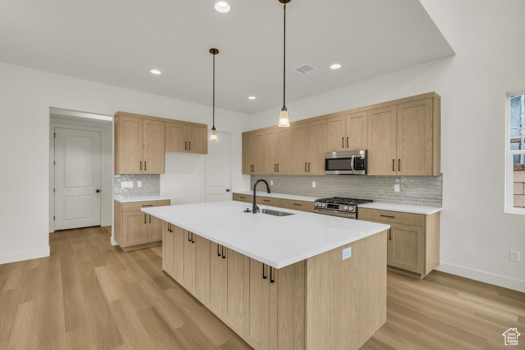 Kitchen featuring decorative light fixtures, light hardwood / wood-style floors, sink, stainless steel appliances, and a center island with sink