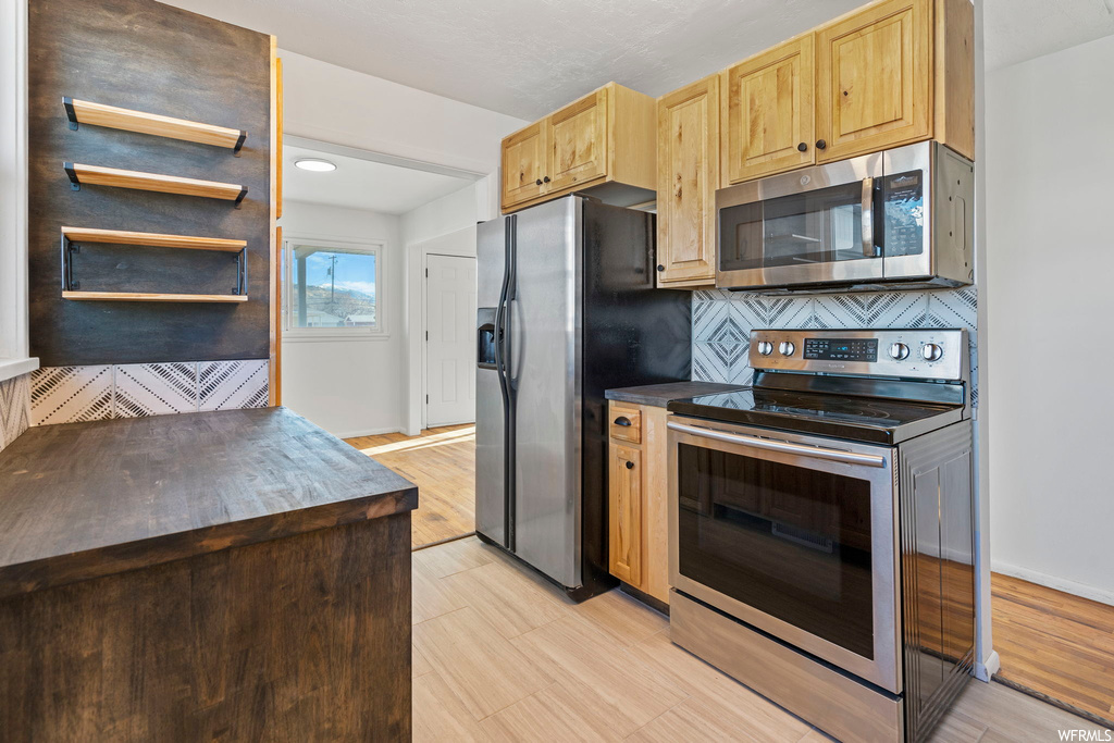 Kitchen featuring tasteful backsplash, light brown cabinets, light wood-type flooring, and stainless steel appliances