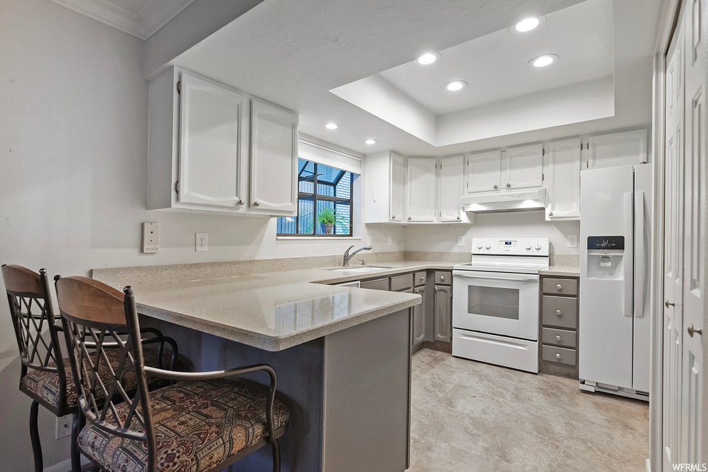 Kitchen with white appliances, a kitchen bar, kitchen peninsula, white cabinets, and a tray ceiling
