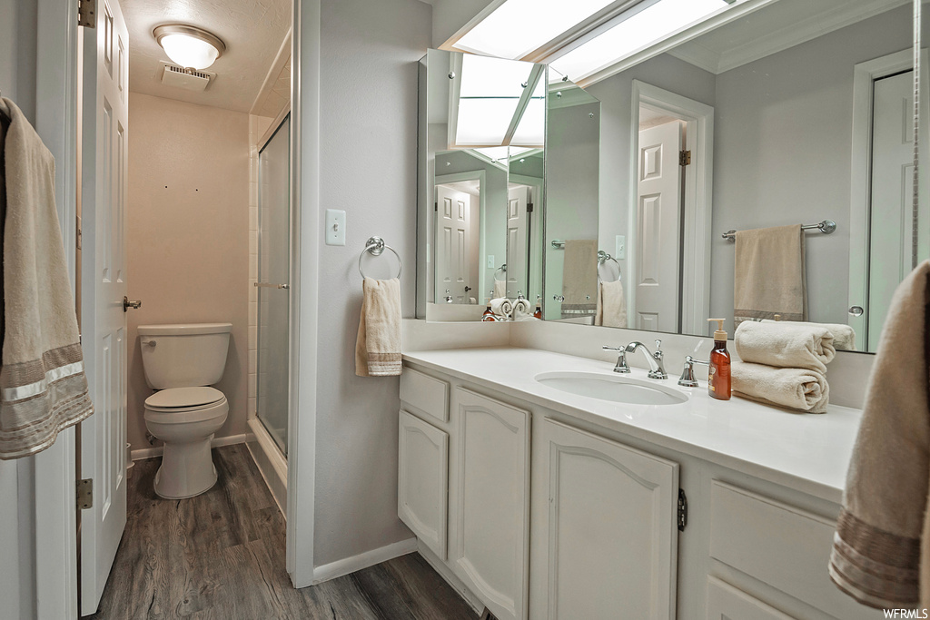 Bathroom with crown molding, a shower with shower door, toilet, wood-type flooring, and vanity with extensive cabinet space