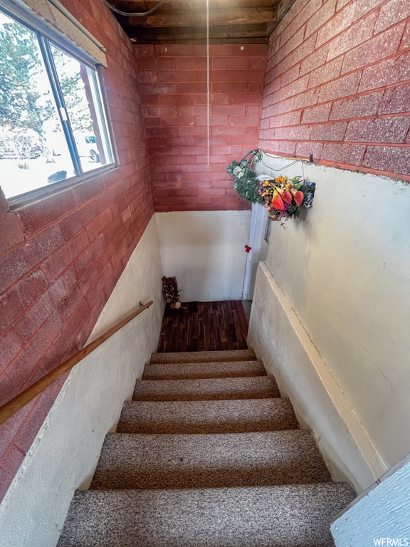 Staircase with dark hardwood / wood-style flooring and brick wall