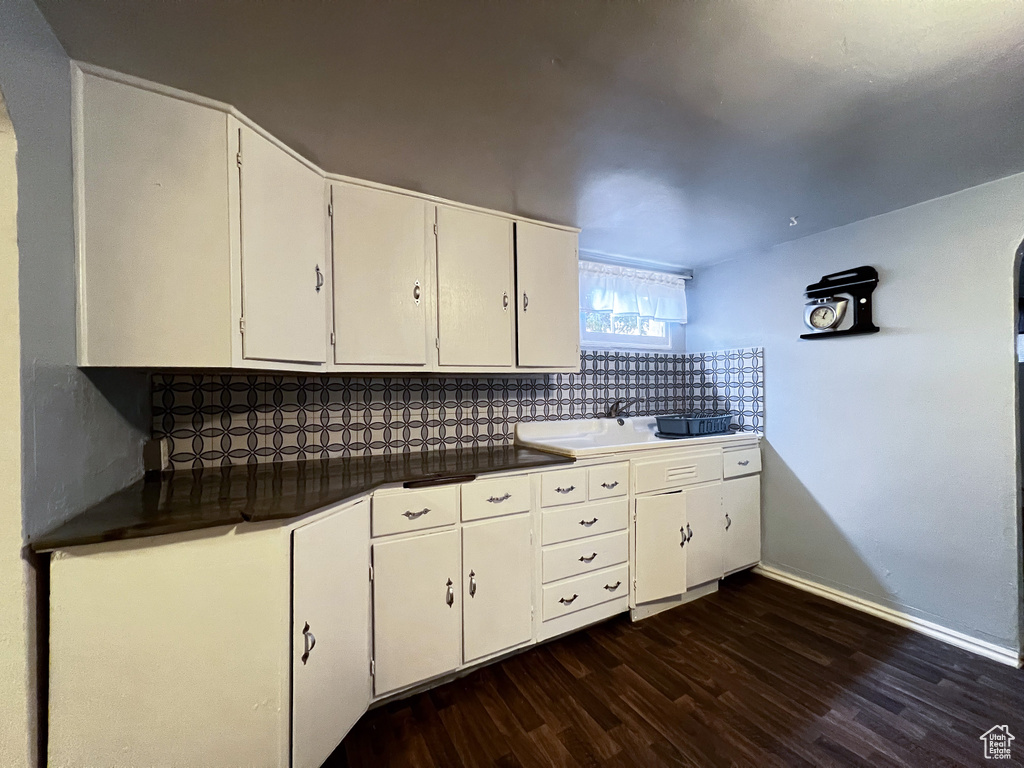 Kitchen featuring sink, backsplash, white cabinetry, and dark wood-type flooring