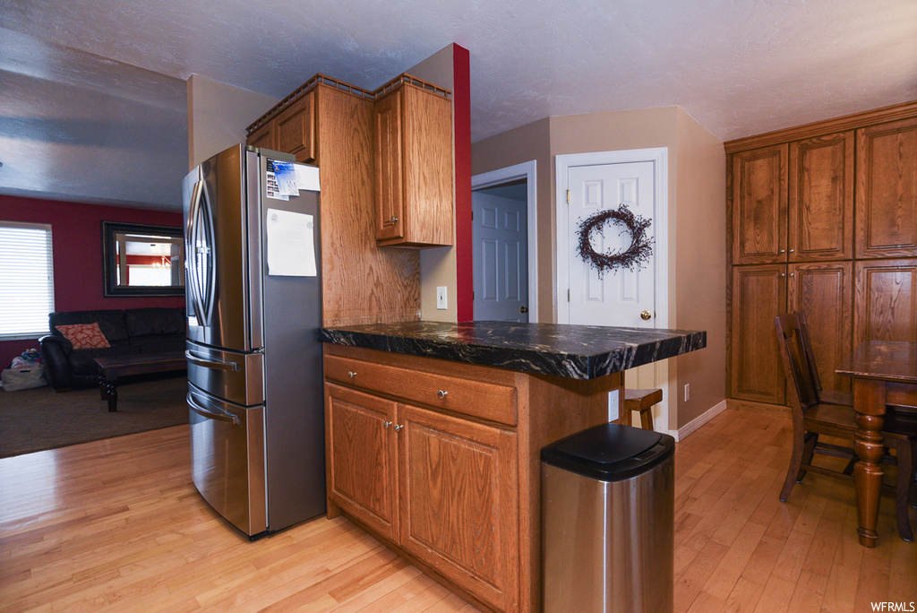 Kitchen featuring stainless steel refrigerator, kitchen peninsula, light wood-type flooring, and dark stone countertops