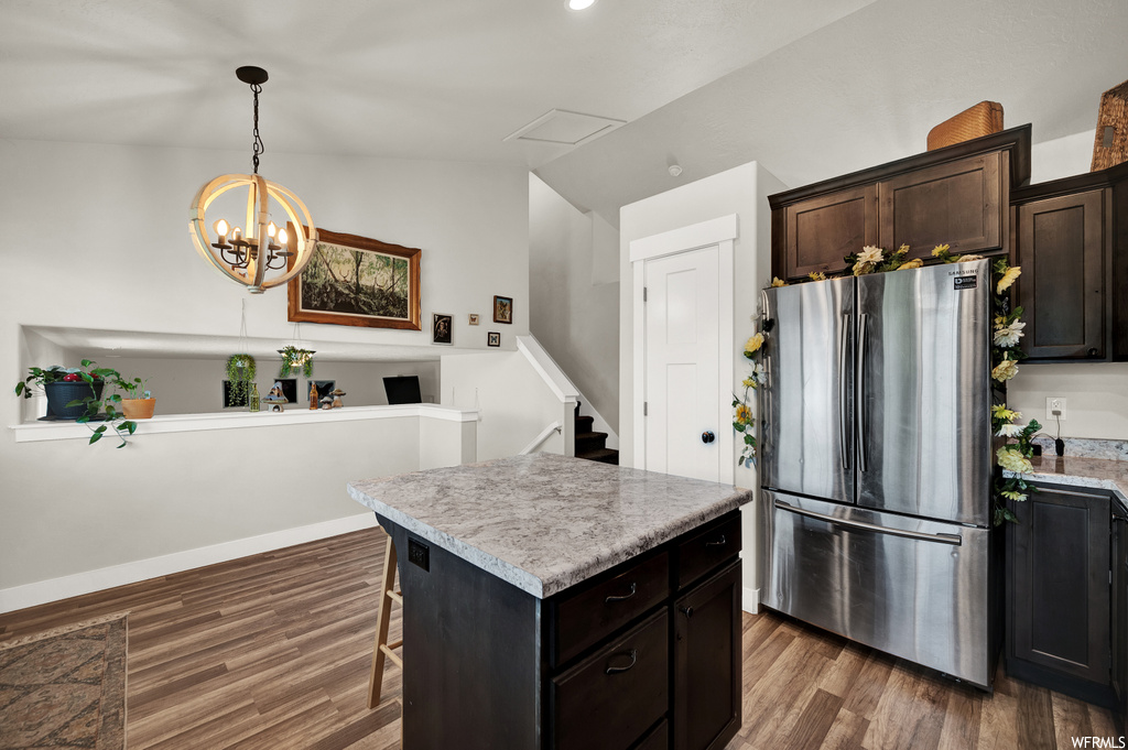 Kitchen featuring hanging light fixtures, stainless steel refrigerator, a kitchen bar, dark wood-type flooring, and a kitchen island