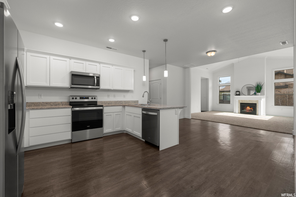 Kitchen with dark hardwood / wood-style flooring, sink, appliances with stainless steel finishes, white cabinets, and decorative light fixtures
