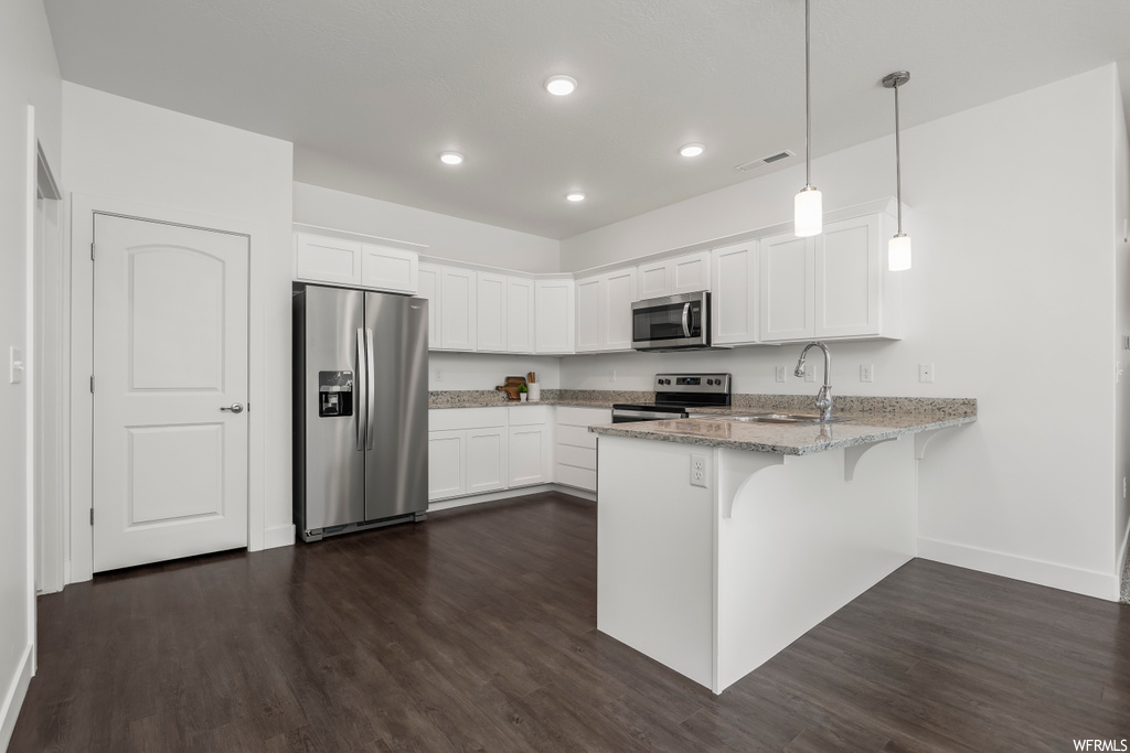 Kitchen with dark hardwood / wood-style floors, white cabinets, decorative light fixtures, and appliances with stainless steel finishes