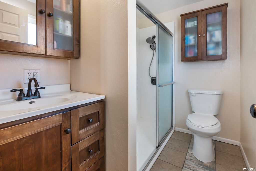 Bathroom with toilet, tile flooring, a shower with door, and vanity