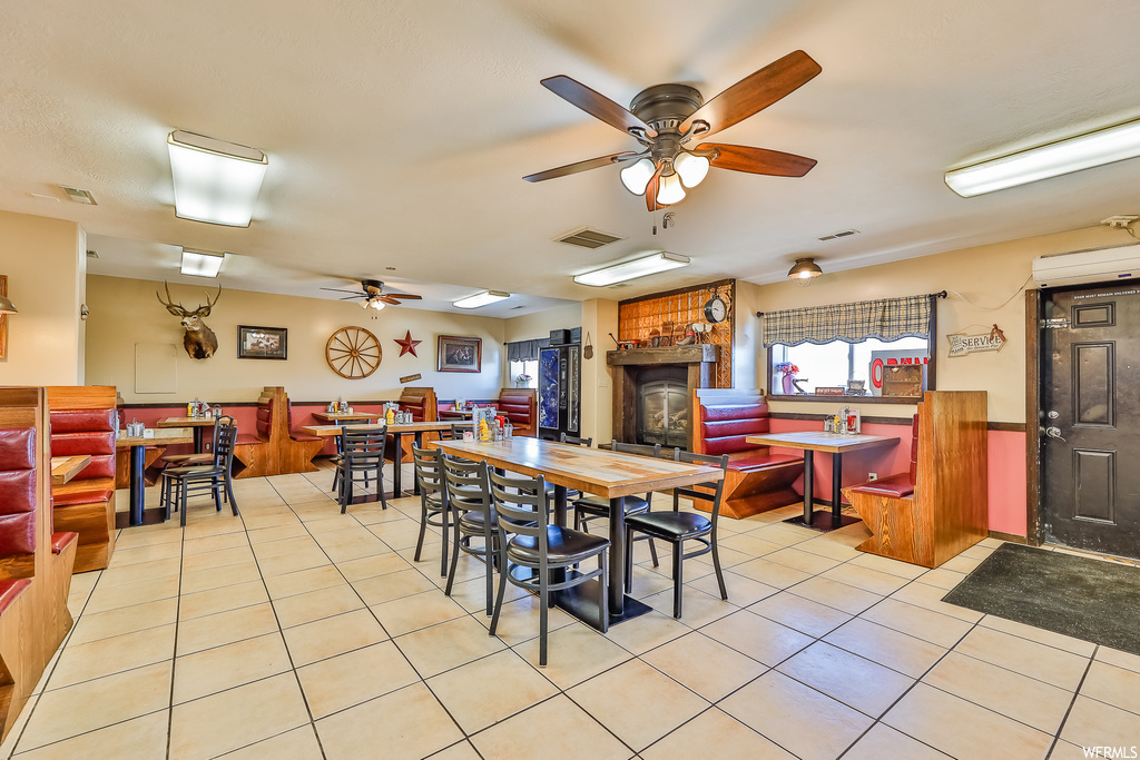 Dining area featuring a wall mounted air conditioner, ceiling fan, a fireplace, and light tile flooring