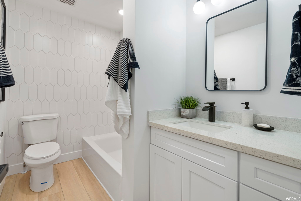 Full bathroom with toilet, hardwood / wood-style flooring, tiled shower / bath, and vanity