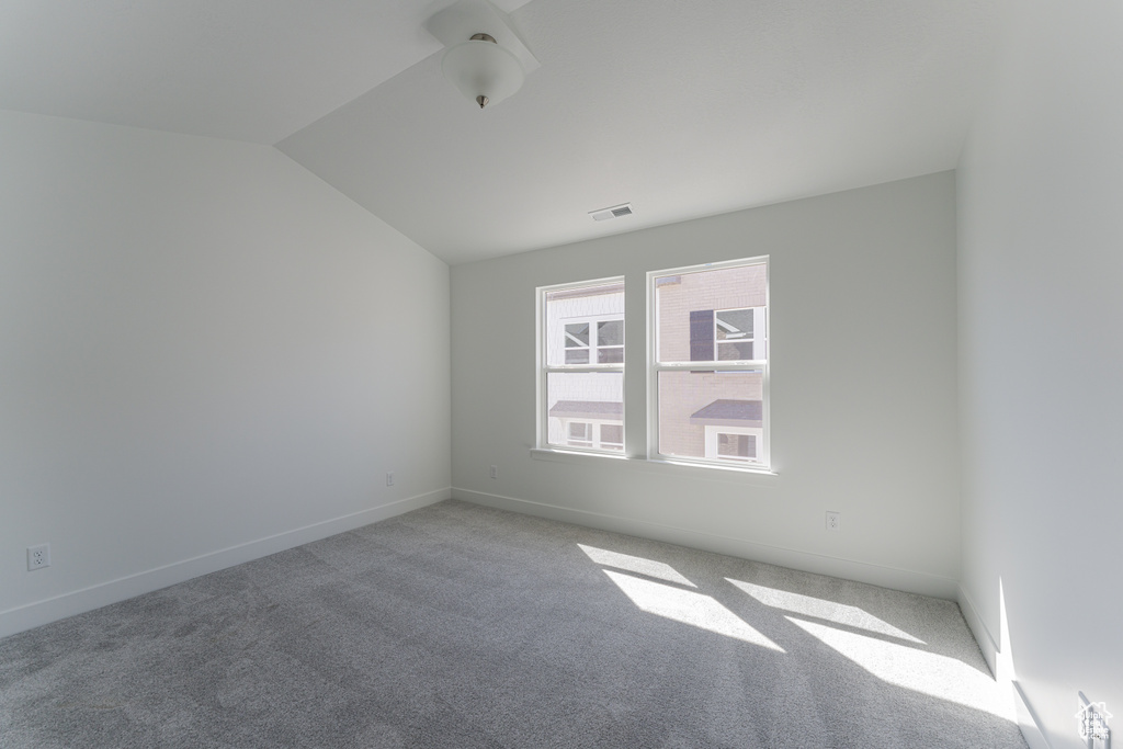 Empty room featuring light colored carpet and lofted ceiling