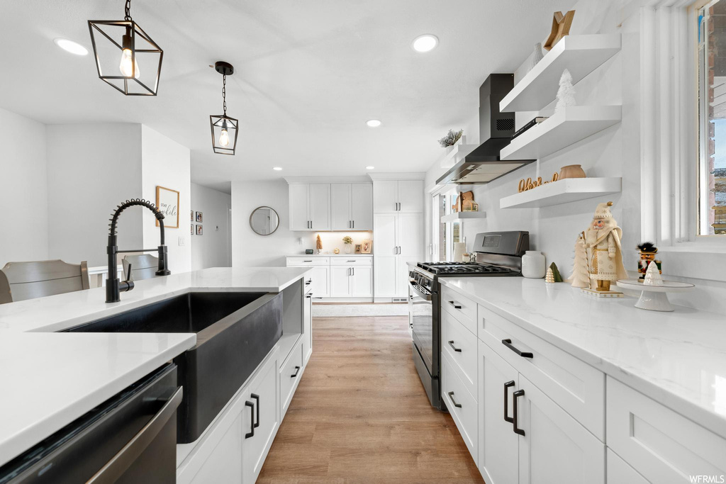 Kitchen with white cabinets, hanging light fixtures, wall chimney range hood, and stainless steel appliances