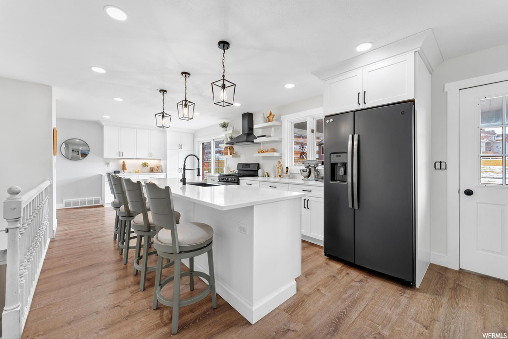Kitchen with wall chimney range hood, light hardwood / wood-style flooring, white cabinets, and stainless steel appliances