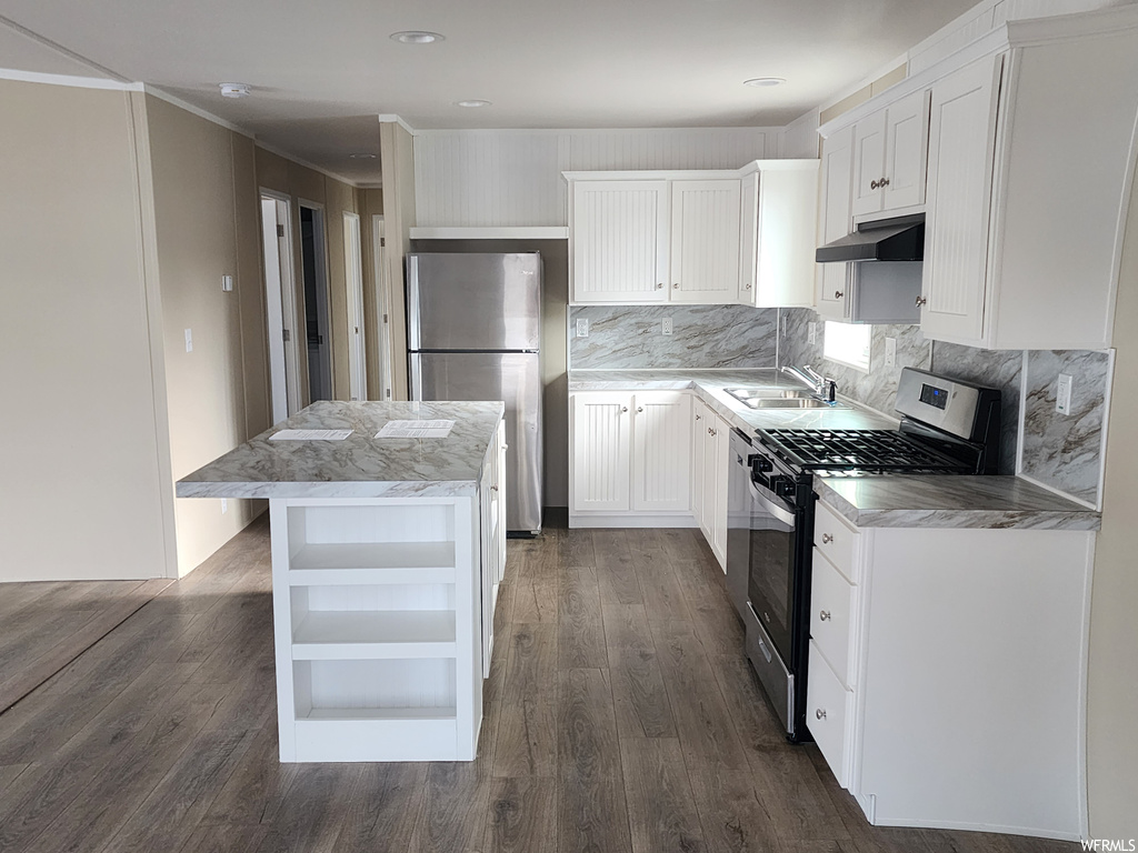 Kitchen with a center island, appliances with stainless steel finishes, dark wood-type flooring, tasteful backsplash, and white cabinetry