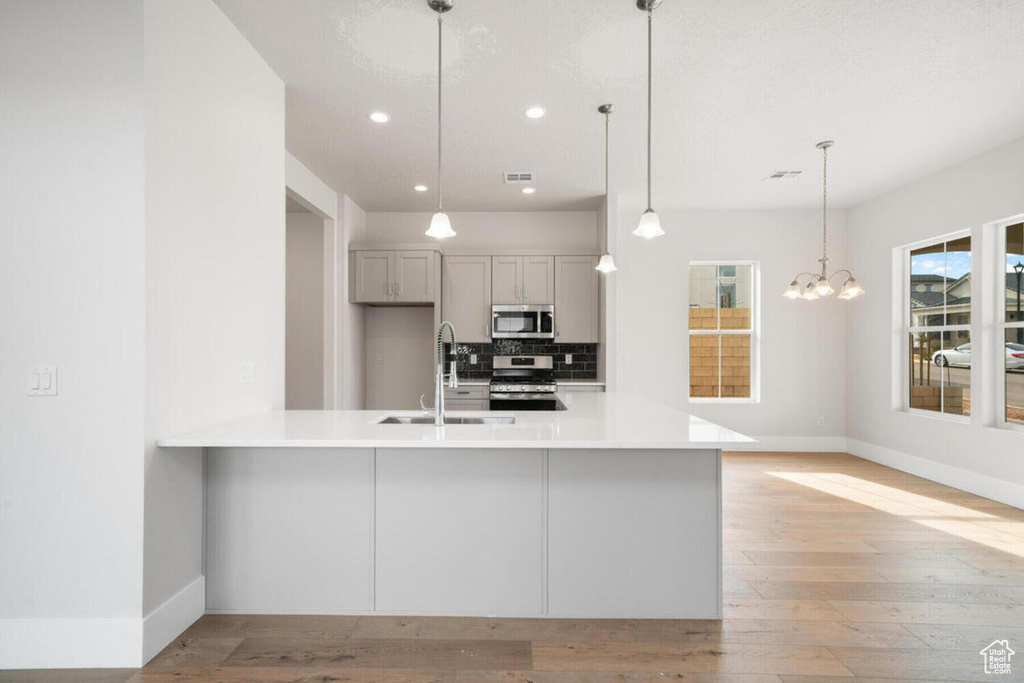 Kitchen featuring sink, hanging light fixtures, stainless steel appliances, tasteful backsplash, and light wood-type flooring