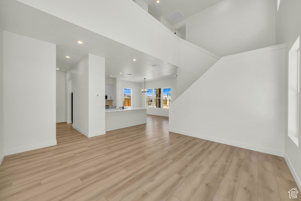 Unfurnished living room featuring light wood-type flooring and a towering ceiling