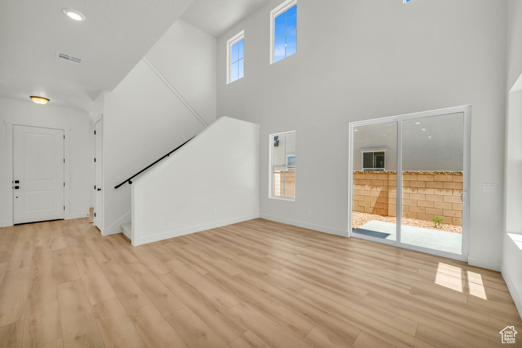 Unfurnished living room featuring a high ceiling, light hardwood / wood-style floors, and a wealth of natural light