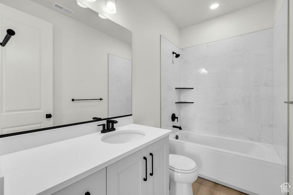 Full bathroom with wood-type flooring, tiled shower / bath, vanity, and toilet