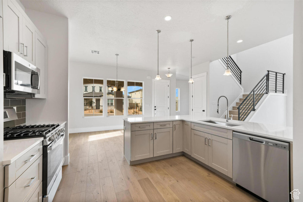 Kitchen featuring a notable chandelier, light hardwood / wood-style floors, sink, stainless steel appliances, and pendant lighting