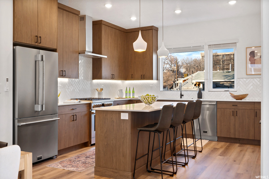 Kitchen featuring hanging light fixtures, light wood-type flooring, high end appliances, and wall chimney exhaust hood