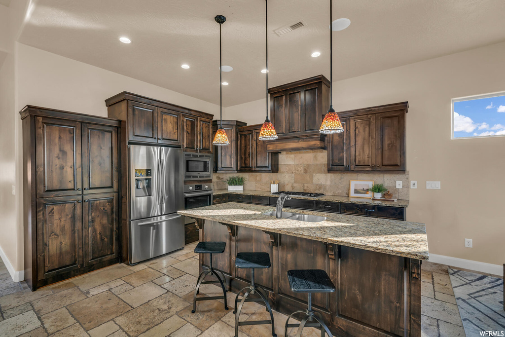 Kitchen with dark brown cabinets, light stone counters, stainless steel appliances, and backsplash