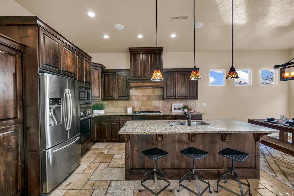 Kitchen with sink, pendant lighting, stainless steel appliances, dark brown cabinetry, and backsplash