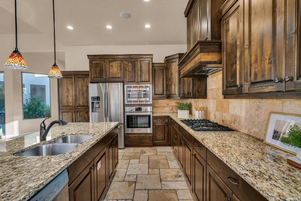 Kitchen with light tile floors, sink, light stone counters, stainless steel appliances, and decorative light fixtures