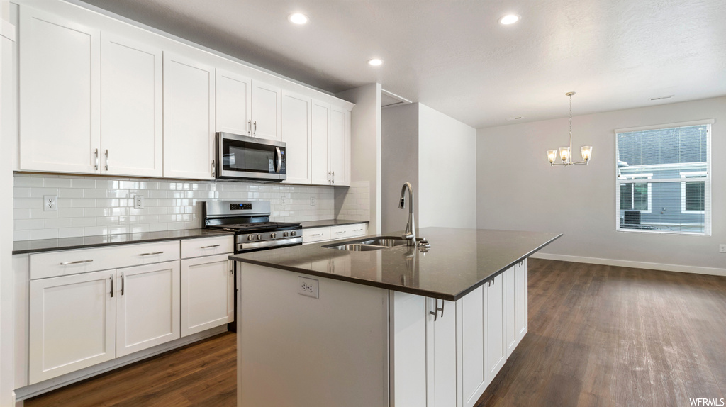 Kitchen featuring white cabinets, dark wood-type flooring, stainless steel appliances, and backsplash