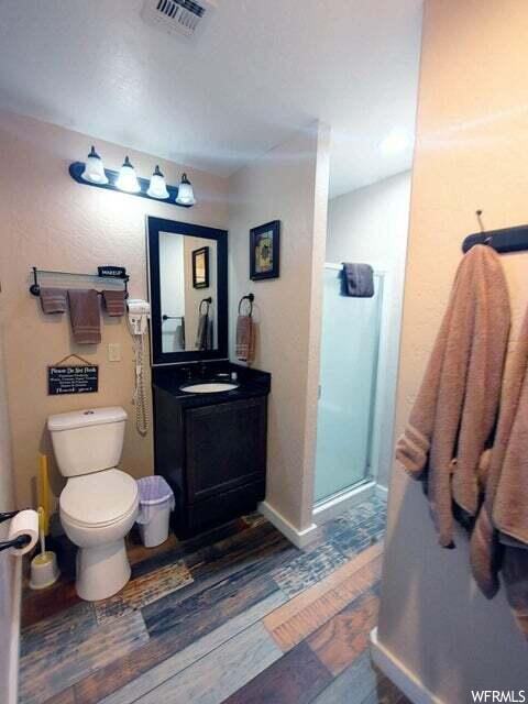 Bathroom featuring toilet, a shower with door, large vanity, and wood-type flooring