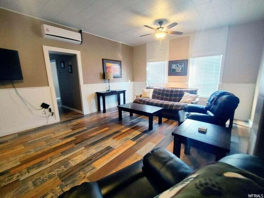 Living room featuring dark hardwood / wood-style flooring, a wall mounted AC, and ceiling fan