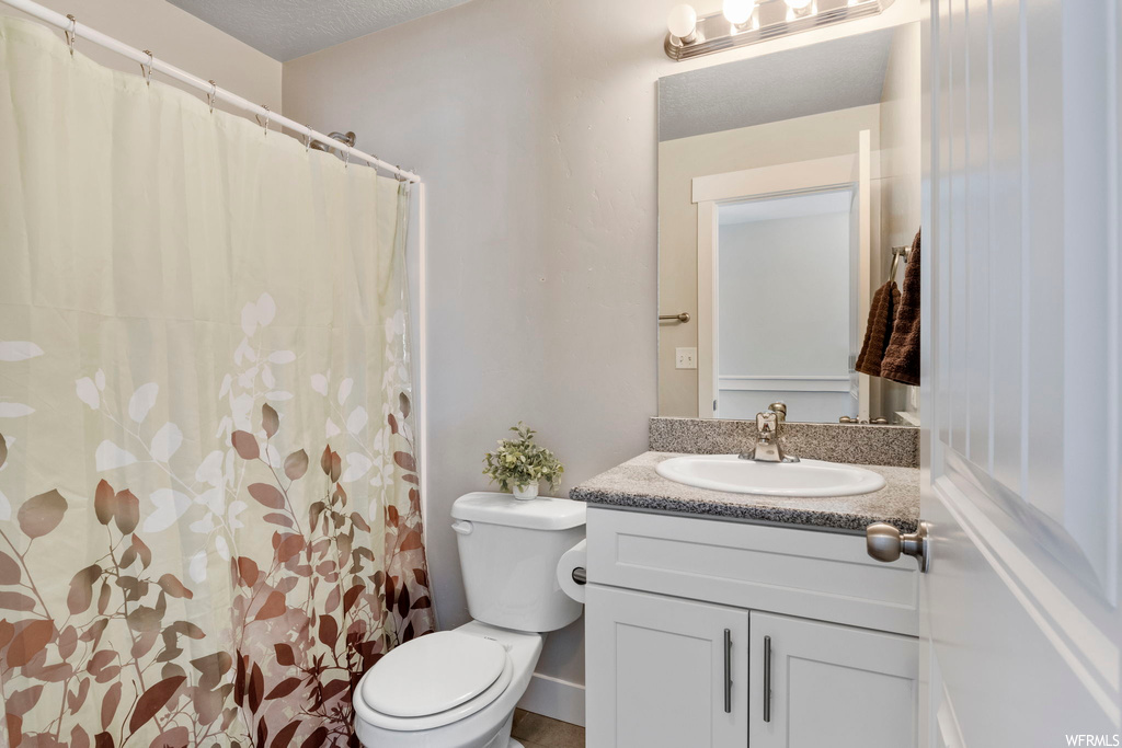 Bathroom with a textured ceiling, vanity, and toilet