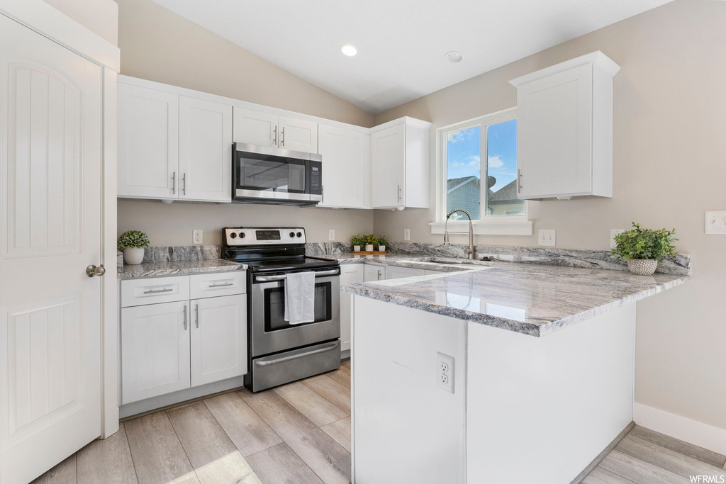 Kitchen with sink, appliances with stainless steel finishes, light stone countertops, white cabinets, and kitchen peninsula