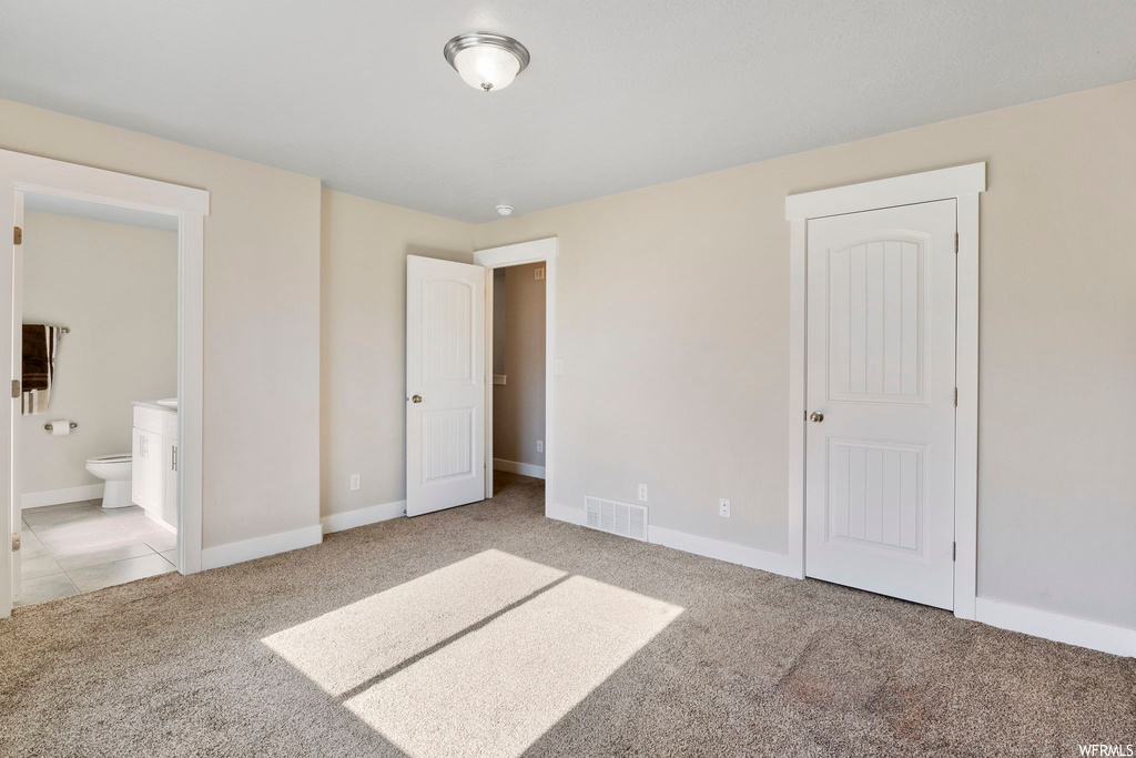 Unfurnished bedroom with connected bathroom, a closet, and light colored carpet