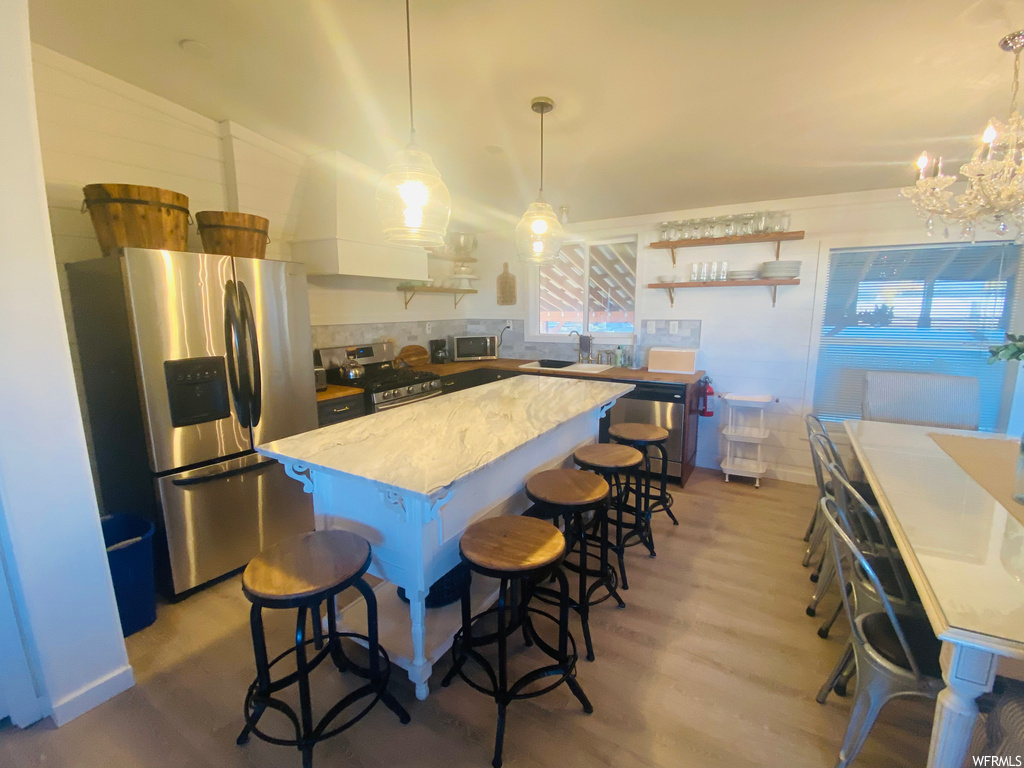 Kitchen featuring light hardwood / wood-style flooring, hanging light fixtures, appliances with stainless steel finishes, a notable chandelier, and a kitchen island