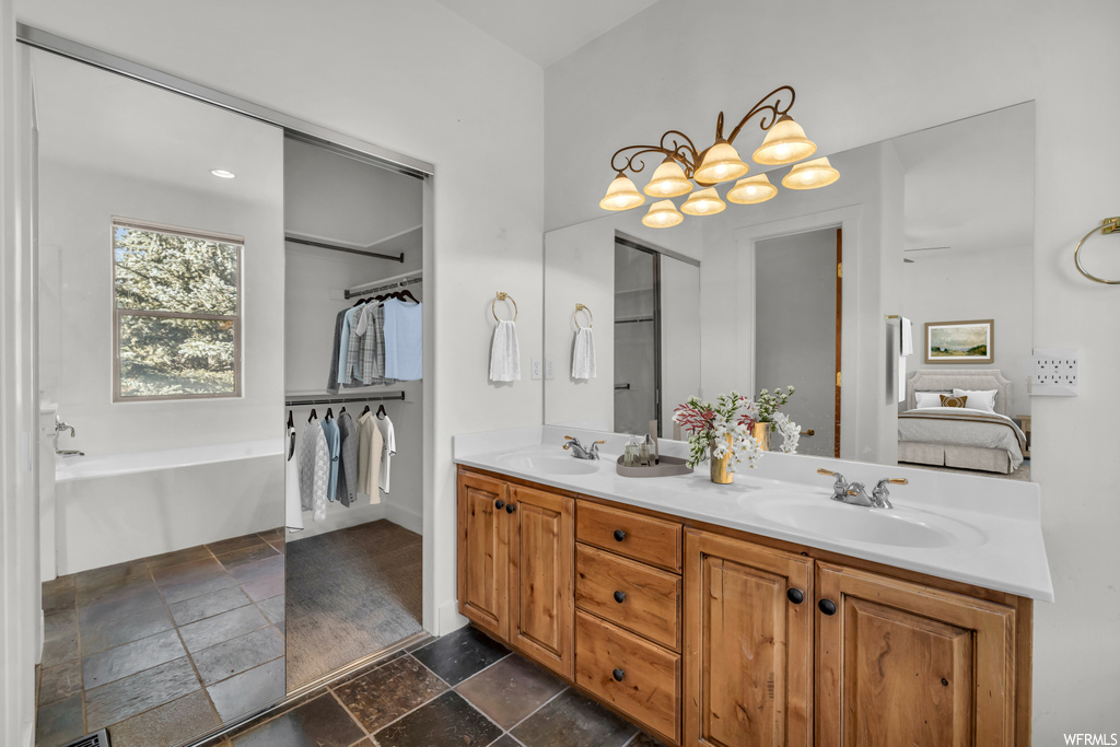 Bathroom featuring an inviting chandelier, tile floors, a bathtub, and dual bowl vanity