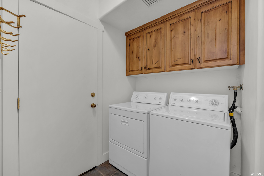 Washroom featuring cabinets, washing machine and dryer, and dark tile flooring