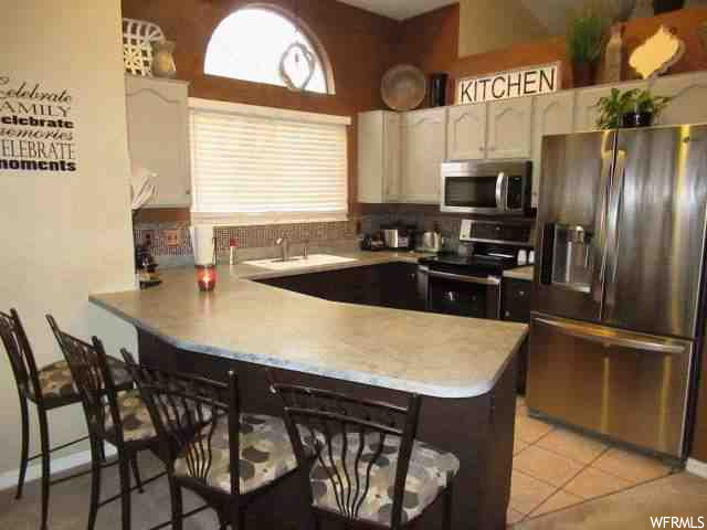 Kitchen with stainless steel appliances, light countertops, backsplash, and light tile floors