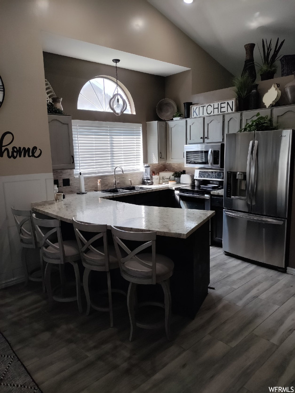 Kitchen featuring dark hardwood floors, decorative light fixtures, backsplash, light countertops, a center island, lofted ceiling, and stainless steel appliances