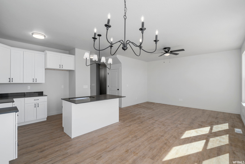 Kitchen with hanging light fixtures, ceiling fan with notable chandelier, white cabinets, light wood-type flooring, and a kitchen island