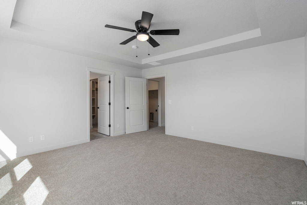 Carpeted empty room with ceiling fan and a raised ceiling