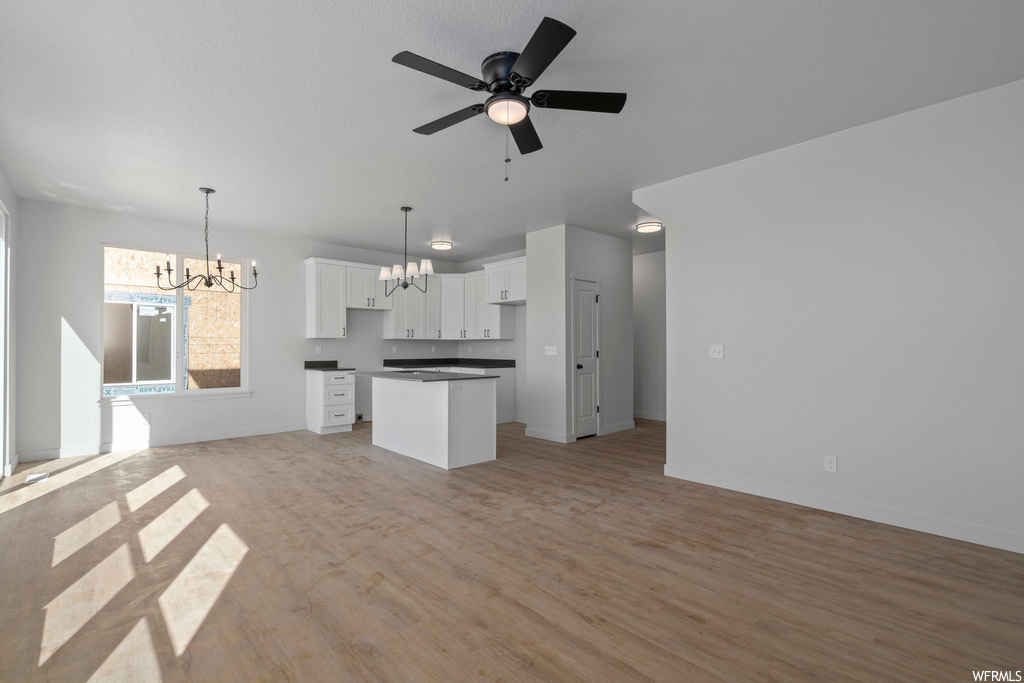 Kitchen with white cabinets, hanging light fixtures, light hardwood / wood-style flooring, and ceiling fan with notable chandelier