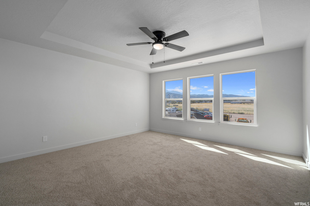 Empty room featuring a raised ceiling, ceiling fan, and light colored carpet