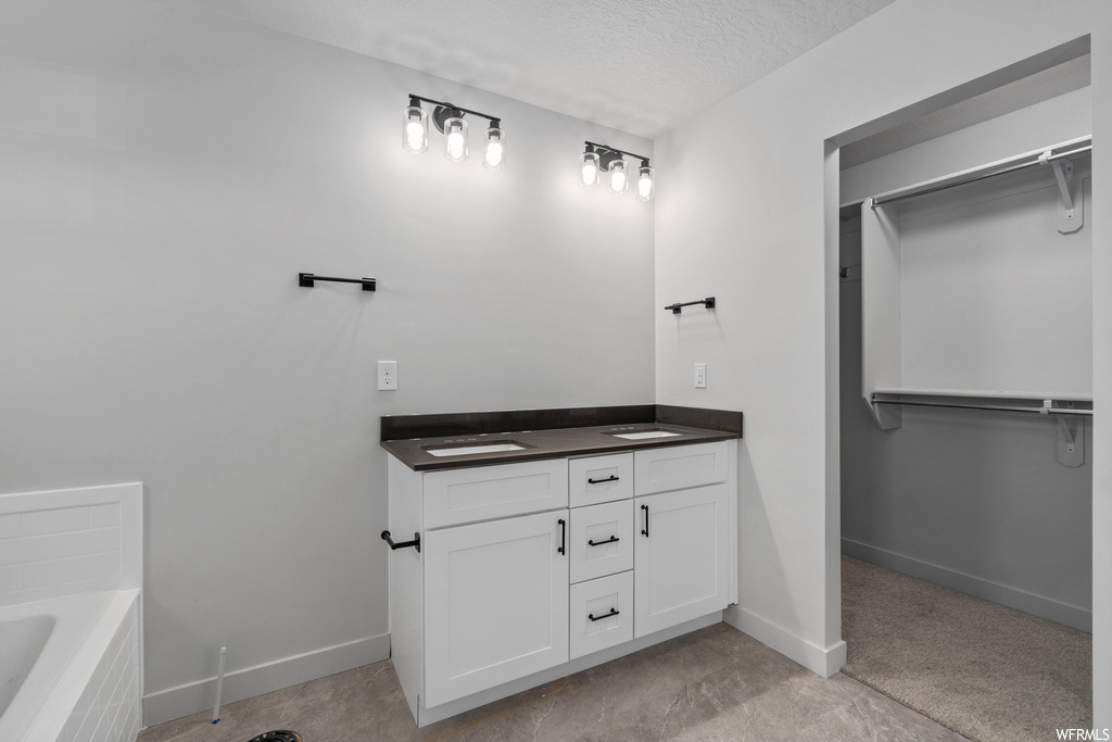 Bathroom featuring a bath to relax in, a textured ceiling, tile floors, and double sink vanity