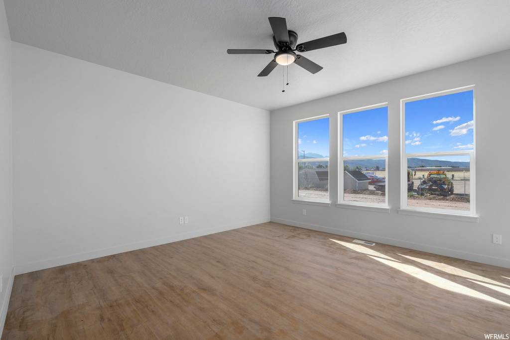 Spare room with ceiling fan, light wood-type flooring, and a healthy amount of sunlight